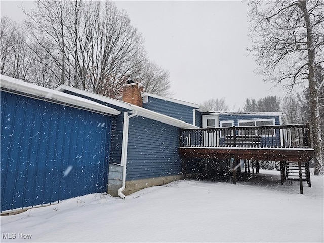 snow covered back of property with a chimney and a deck