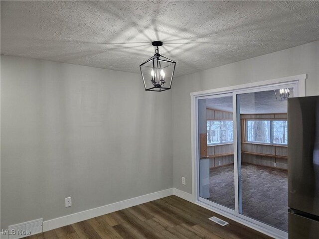 unfurnished dining area with a textured ceiling, visible vents, baseboards, dark wood-style floors, and an inviting chandelier