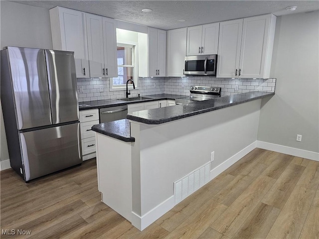 kitchen with stainless steel appliances, dark countertops, visible vents, white cabinets, and a peninsula