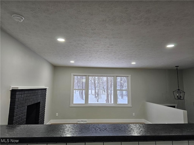 unfurnished living room featuring recessed lighting, visible vents, a brick fireplace, a textured ceiling, and baseboards