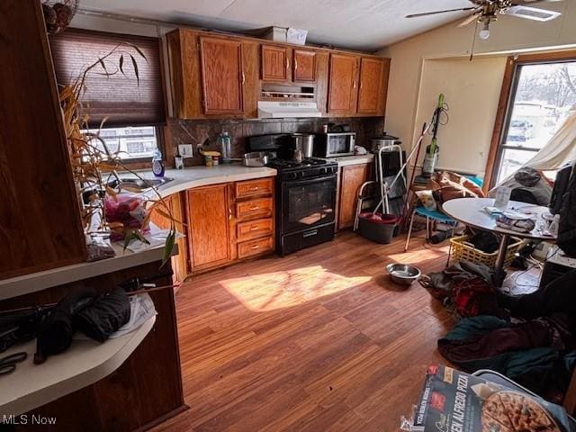 kitchen featuring brown cabinetry, a wealth of natural light, light countertops, and black gas stove