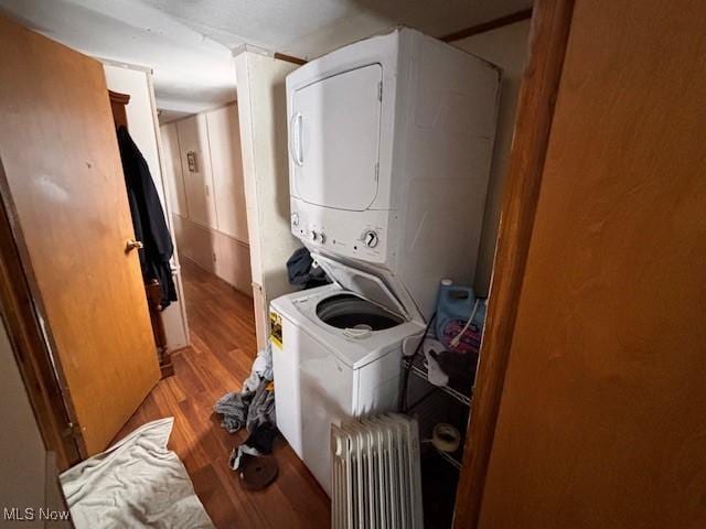 clothes washing area with laundry area, light wood finished floors, stacked washer and clothes dryer, and radiator