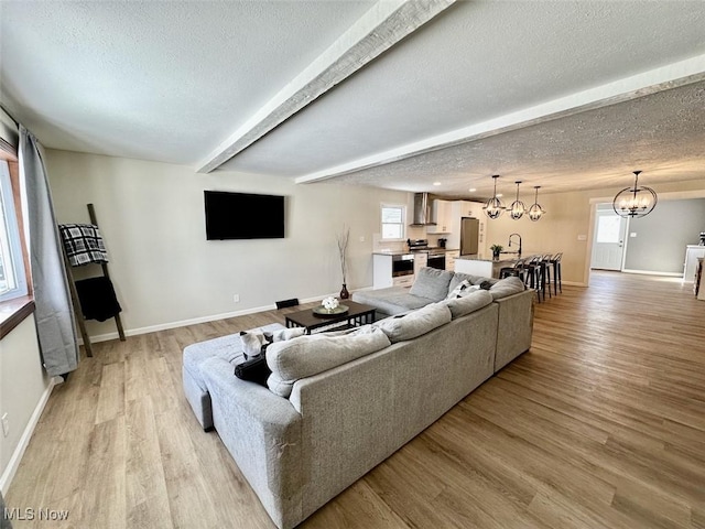 living room with beam ceiling, a notable chandelier, a textured ceiling, and light wood finished floors