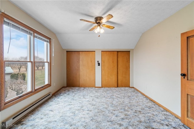 unfurnished bedroom featuring vaulted ceiling, a textured ceiling, baseboard heating, carpet floors, and multiple closets