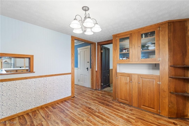 interior space with a textured ceiling, light wood finished floors, wainscoting, and an inviting chandelier