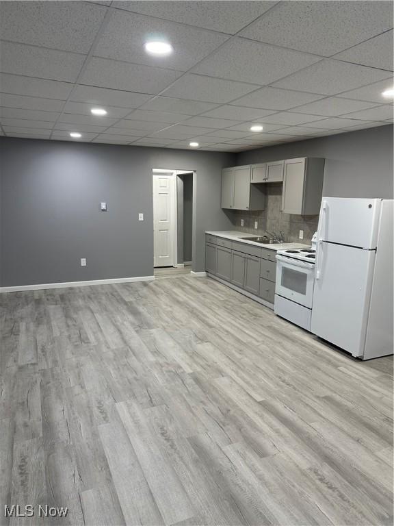 kitchen featuring light wood finished floors, gray cabinets, light countertops, white appliances, and baseboards