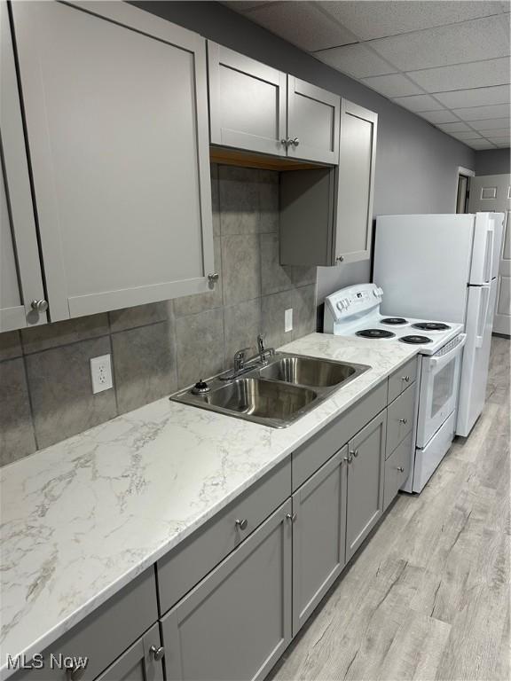 kitchen featuring light wood finished floors, gray cabinets, light countertops, white appliances, and baseboards