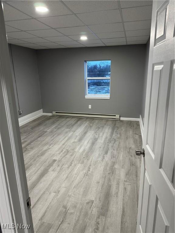 empty room featuring light wood-style floors, baseboards, a drop ceiling, and baseboard heating