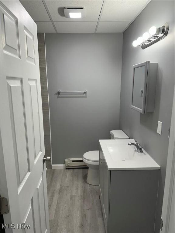 bathroom featuring a drop ceiling, toilet, wood finished floors, baseboard heating, and vanity