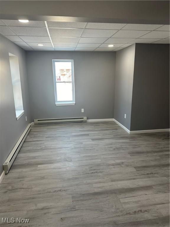 empty room featuring light wood finished floors, a baseboard radiator, a paneled ceiling, and baseboards