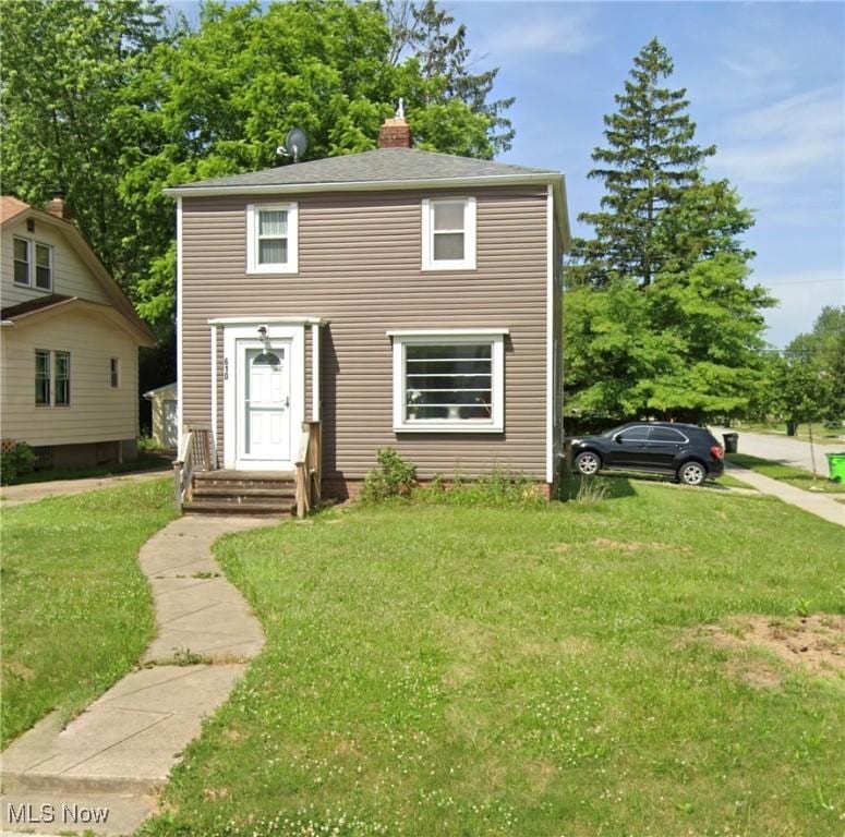 view of front of house with entry steps, a chimney, and a front lawn