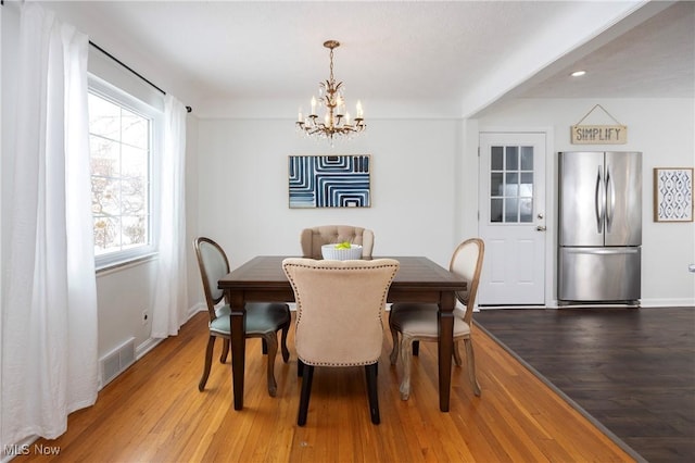 dining room with an inviting chandelier, baseboards, visible vents, and wood finished floors