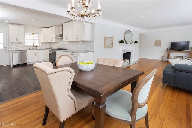 dining room with light wood-style floors, recessed lighting, a notable chandelier, and a fireplace with flush hearth