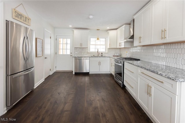 kitchen with wall chimney range hood, white cabinetry, pendant lighting, and stainless steel appliances