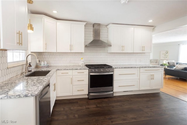 kitchen featuring stainless steel appliances, hanging light fixtures, open floor plan, a sink, and wall chimney range hood