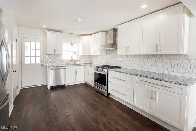 kitchen with pendant lighting, stainless steel appliances, white cabinets, a sink, and wall chimney exhaust hood