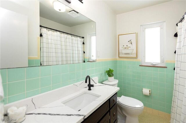 full bath with tile walls, visible vents, toilet, wainscoting, and vanity