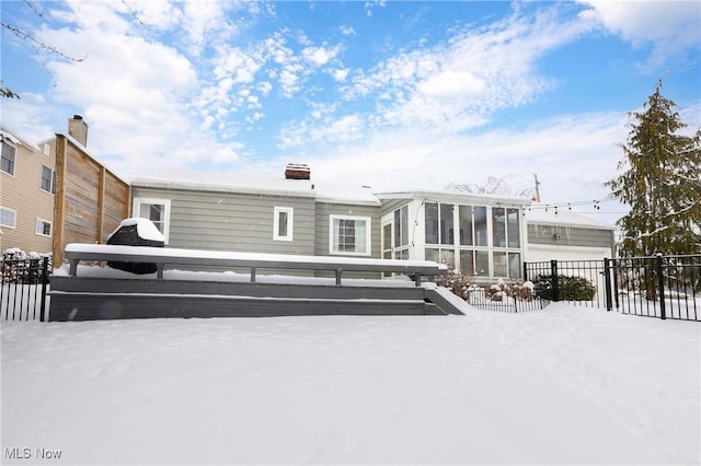 snow covered property with fence and a sunroom