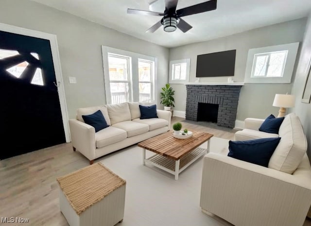 living area featuring light wood-type flooring, ceiling fan, a fireplace, and baseboards