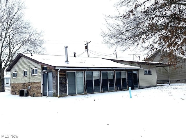 snow covered property with central AC and brick siding