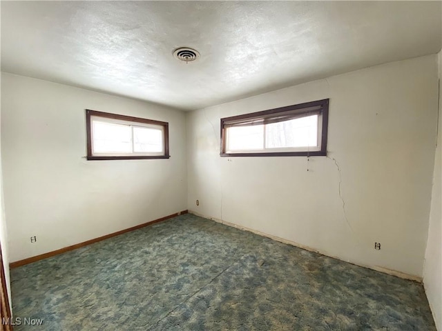 empty room with visible vents, dark carpet, and baseboards