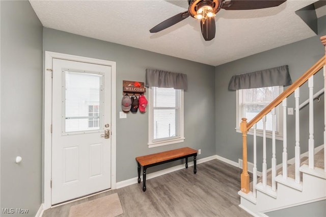 entrance foyer with baseboards, a ceiling fan, stairway, a textured ceiling, and light wood-type flooring