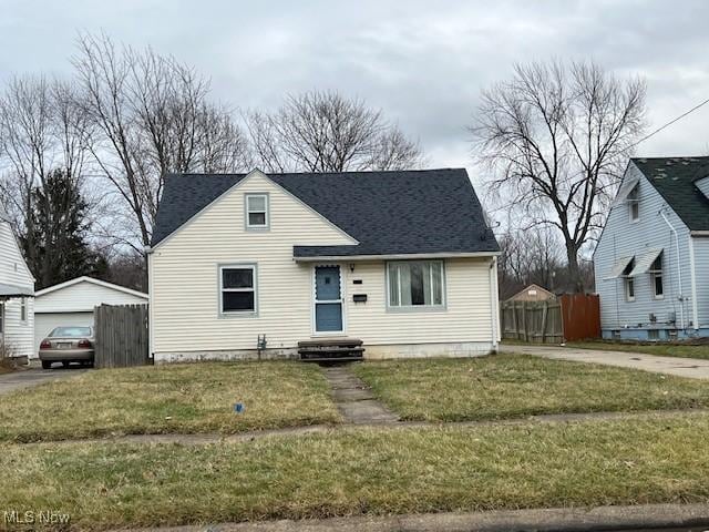 view of front of house featuring roof with shingles, fence, a front lawn, and an outdoor structure