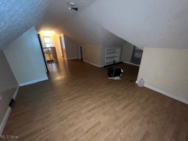 bonus room featuring vaulted ceiling, a textured ceiling, baseboards, and wood finished floors