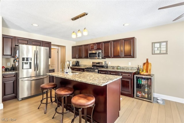 kitchen with beverage cooler, stainless steel appliances, a breakfast bar, a sink, and an island with sink