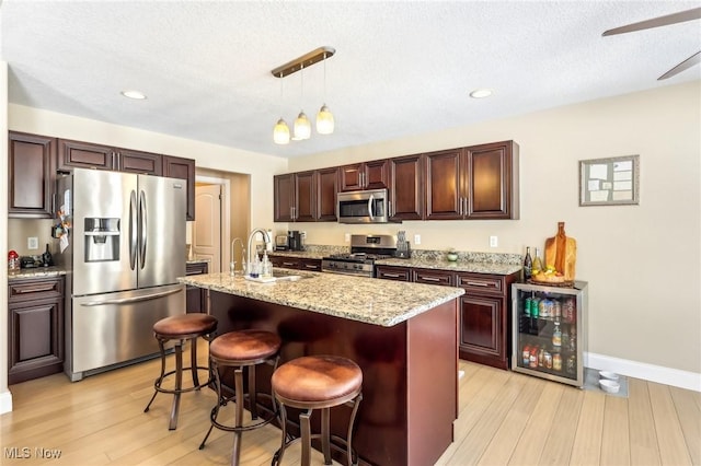kitchen with a sink, light wood-type flooring, stainless steel appliances, pendant lighting, and beverage cooler