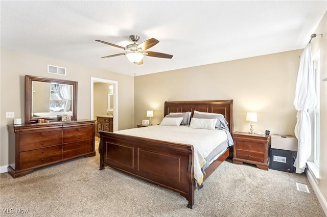 bedroom with ensuite bathroom, a ceiling fan, visible vents, and light colored carpet