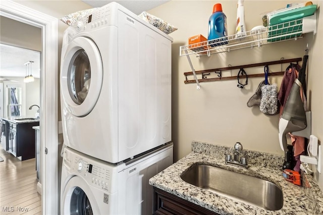 laundry area featuring a sink, laundry area, stacked washer and clothes dryer, and light wood-style floors