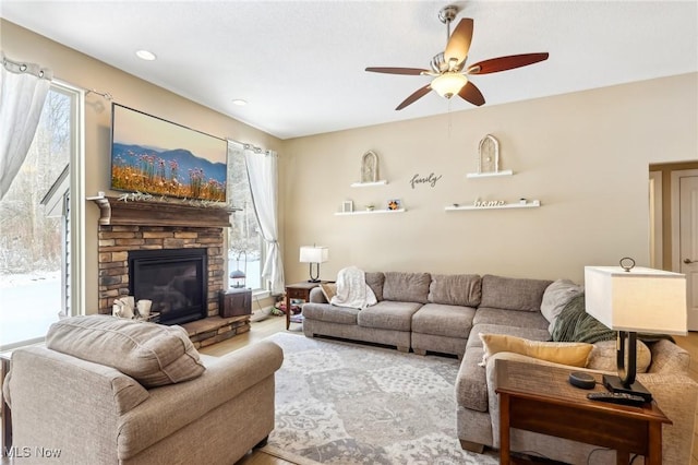 living room featuring wood finished floors, ceiling fan, and a stone fireplace