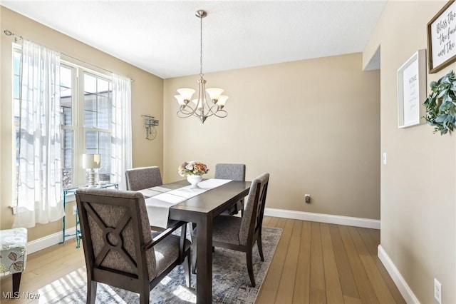 dining area with baseboards, light wood-type flooring, and a chandelier