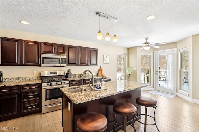 kitchen with a kitchen island with sink, a kitchen breakfast bar, appliances with stainless steel finishes, light wood-type flooring, and pendant lighting