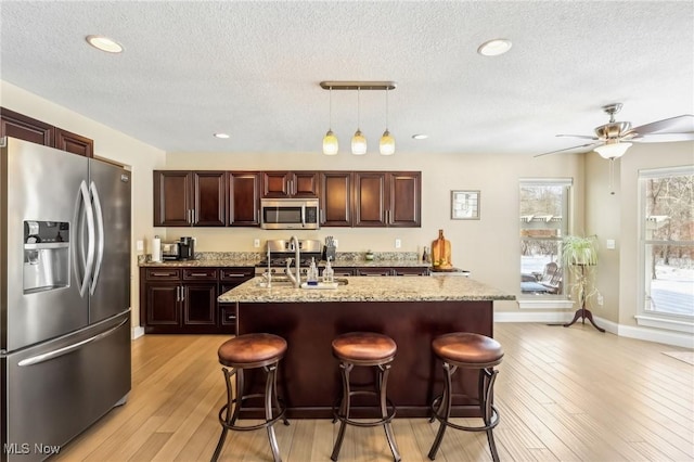 kitchen with stainless steel appliances, light wood finished floors, a textured ceiling, and a sink
