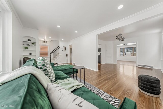 living room with built in shelves, wood finished floors, baseboards, stairs, and crown molding