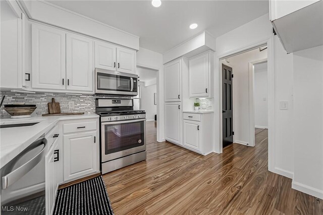 kitchen featuring white cabinets, stainless steel appliances, light countertops, light wood-style floors, and backsplash