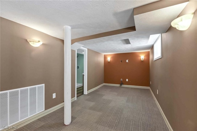 finished below grade area with carpet, visible vents, a textured ceiling, and baseboards