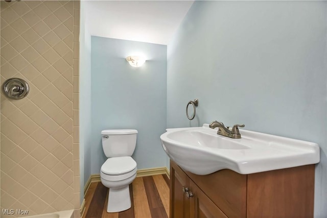 bathroom featuring toilet, wood finished floors, vanity, baseboards, and walk in shower