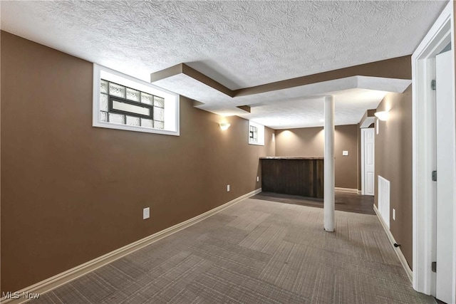 below grade area featuring a textured ceiling, baseboards, and carpet flooring