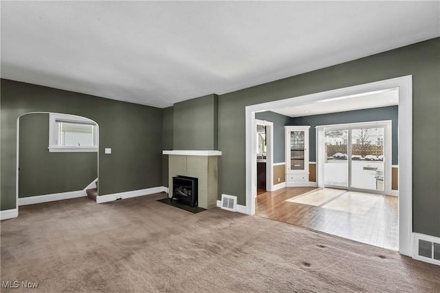 unfurnished living room featuring baseboards, visible vents, arched walkways, and carpet flooring