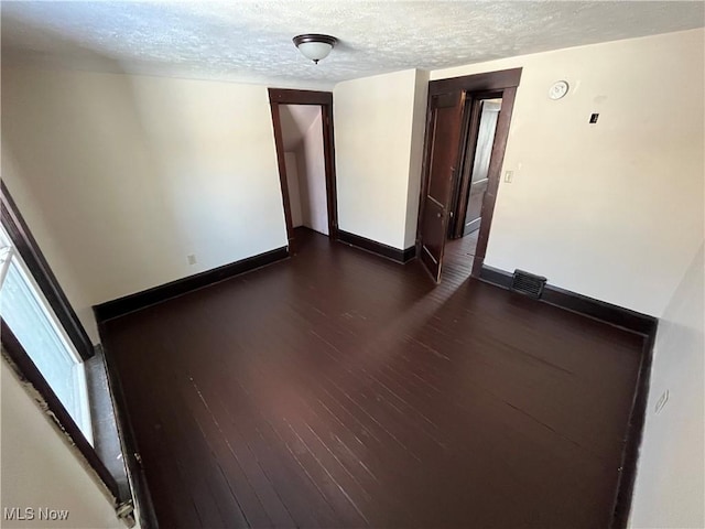 spare room featuring visible vents, baseboards, dark wood-style flooring, and a textured ceiling