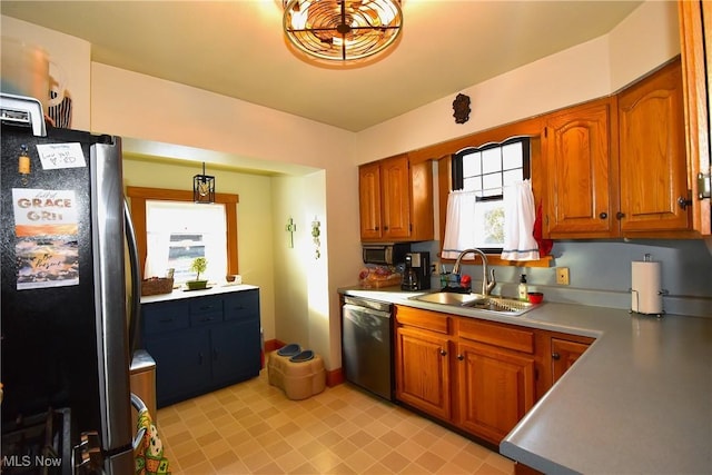 kitchen featuring stainless steel appliances, a sink, light countertops, brown cabinetry, and decorative light fixtures