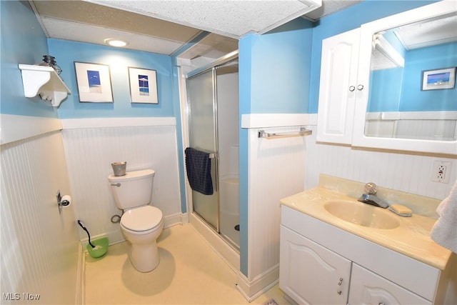 bathroom with a wainscoted wall, toilet, a shower stall, and vanity