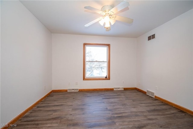 spare room with dark wood-style flooring, visible vents, and baseboards