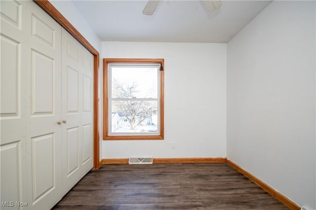 unfurnished bedroom featuring dark wood-style flooring, a closet, visible vents, ceiling fan, and baseboards