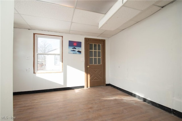 empty room featuring a paneled ceiling, baseboards, and wood finished floors