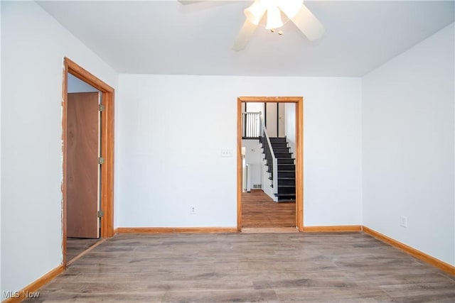 spare room with ceiling fan, stairway, wood finished floors, and baseboards