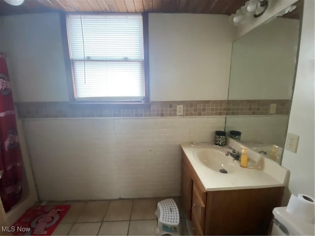 bathroom featuring vanity, a shower with curtain, wainscoting, tile patterned floors, and tile walls